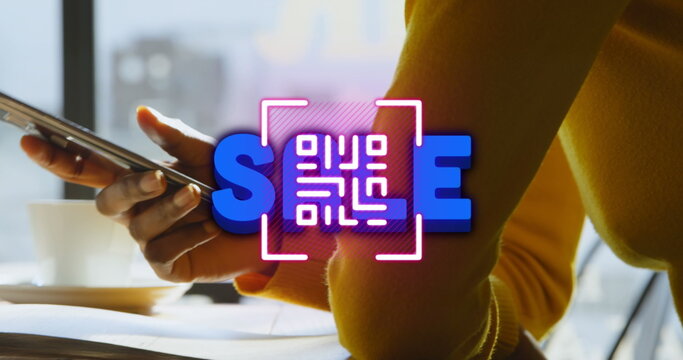 Woman in yellow top holding smartphone at desk by window, with neon QR code spelling SCAN