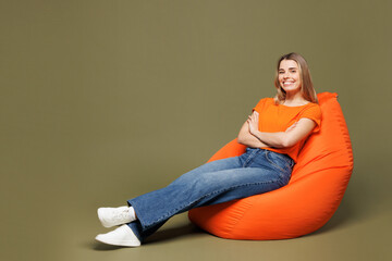 Full body young smiling woman wears orange t-shirt casual clothes sit in bag chair hold hands...
