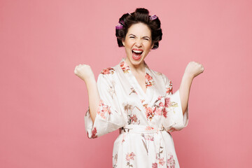 Young housewife housekeeper woman she wears white robe hair rollers doing winner gesture celebrate...