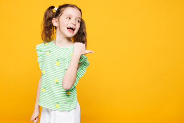 Little smiling fun cute kid child girl 8-9 years old wears green t-shirt point thumb finger back...