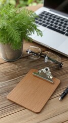 A minimalistic office desk displays a clipboard with blank paper, a laptop, stylish glasses, and green plants, creating an inviting and productive workspace atmosphere.
