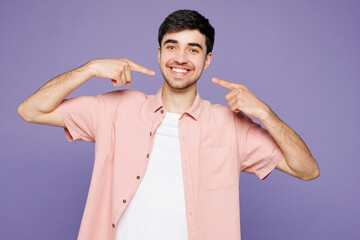 Young smiling cheerful fun man he wears pink shirt t-shirt casual clothes point index fingers on...