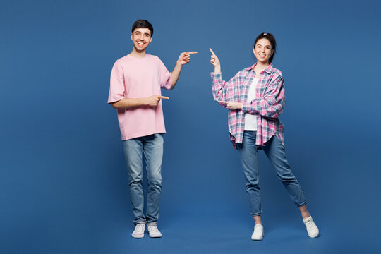 Fototapeta Full body young smiling couple two friends family man woman they wear pink casual clothes together point index finger on area between them isolated on plain blue background studio. Lifestyle concept.