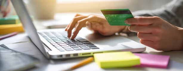 The hands holding a credit card while shopping online at a laptop.