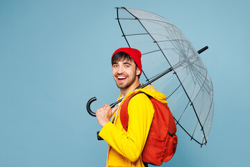 Side view traveler man wear hat yellow raincoat casual clothes hold umbrella isolated on plain blue...
