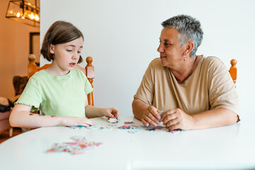 Grandmother and granddaughter doing puzzle at home.