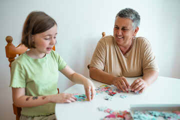 Grandmother and granddaughter doing puzzle at home.