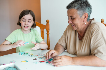 Grandmother and granddaughter doing puzzle at home.