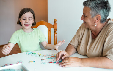 Grandmother and granddaughter doing puzzle at home.
