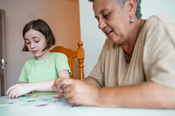 Grandmother and granddaughter doing puzzle at home.