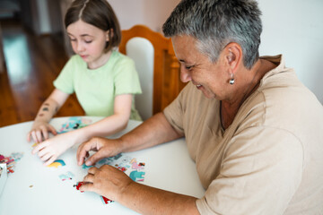 Grandmother and granddaughter doing puzzle at home.