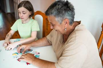 Grandmother and granddaughter doing puzzle at home.