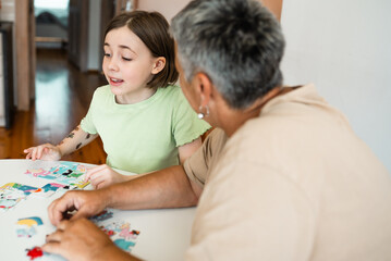 Grandmother and granddaughter doing puzzle at home.