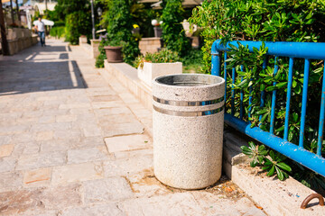 Naklejka premium Urban stone trash bin on sunny pedestrian walkway. Clean environment, public infrastructure, and cityscape details.