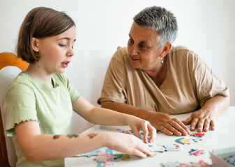 Grandmother and granddaughter doing puzzle at home.