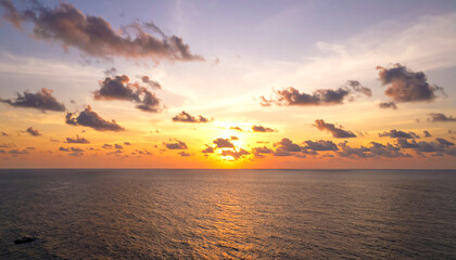 Obraz premium A stunning sunset over the ocean, with vibrant orange and yellow hues blending into the serene blue water and fluffy clouds scattered across the sky