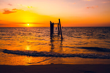 The view of the old wooden bridge decayed in the middle of the ocean in the evening. The sun is...
