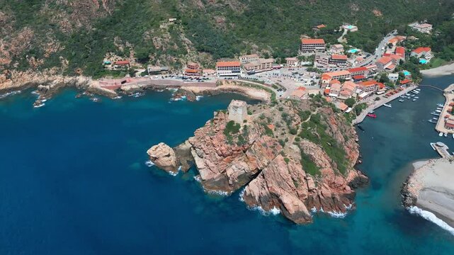 Aerial view circling the Genoise tower on a rocky outcrop, the beach and town of Porto on the west coast of the Mediterranean island of Corsica with mountains behind