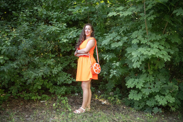 Portrait of a young beautiful girl in an orange dress in a summer forest.