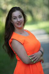 Portrait of a young beautiful girl in an orange dress in a summer forest.
