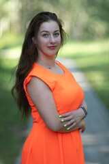 Portrait of a young beautiful girl in an orange dress in a summer forest.