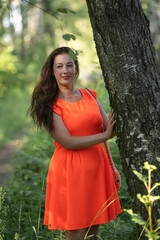 Portrait of a young beautiful girl in an orange dress in a summer forest.