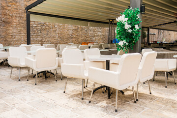 Outdoor cafe terrace with white chairs and floral decor. Hospitality atmosphere, modern leisure space, and Mediterranean dining culture.
