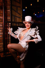 Performer in a sparkling costume and white top hat posing for the camera. Bright stage look in...