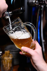 The photo captures the moment a glass of fresh light beer is being filled from a tap. The mug is...