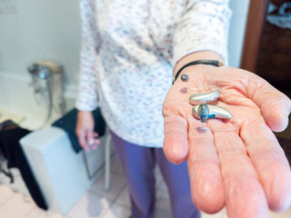 Elderly person holding a pair hearing aids in hand. assistive hearing technology in real-life setting, highlighting accessibility, senior healthcare, hearing loss. Bathroom, emphasizing daily use and 