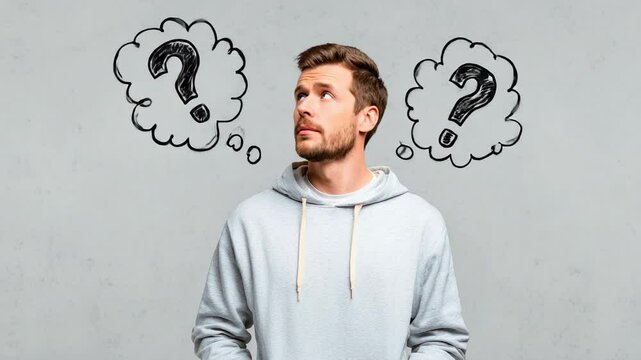 Thoughtful man in hoodie looking up with question marks in doodle clouds on gray background confusion