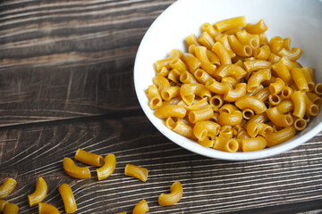 a bowl of raw elbow pasta placed neatly on a rustic wooden table