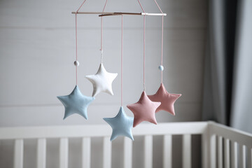 Soft pastel star mobile hanging above crib nursery decor baby room calming atmosphere gentle colors plush fabric blue pink white peaceful modern style