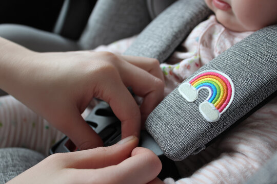 Baby car seat safety hands buckle close up rainbow embroidery infant secure gray fabric child protection transportation seatbelt soft comfort clothing pattern Buckling baby into car seat with gray - Powered by Adobe