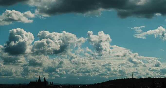 Time-lapse video scenery with the silhouette of Prague Castle and Petř&iacute;n Lookout Tower against a blue sky with dynamic fluffy white clouds