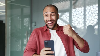 Happy excited businessman celebrates success by reading great news on mobile phone sitting at workplace in business office. Smiling shocked surprised worker received a positive good message. Close up - Powered by Adobe