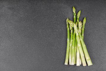 Bunch of raw fresh green asparagus stalks macro, close up on black textured background with copy...
