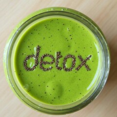 Top view of green detox smoothie in glass jar with chia seeds spelling the word detox on the surface, placed on light wooden table