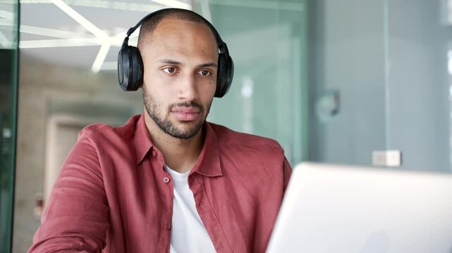 Focused businessman or IT specialist in wireless headphones works on a laptop sitting at workplace in business office. Serious coder developer is programming, busy with a project on computer. Close up