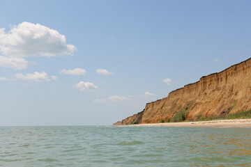 A serene wide shot of a sandy beach stretching along the base of towering, layered cliffs, with a...