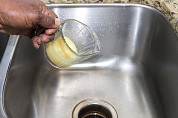 A person pouring  old cooking grease in a kitchen sink