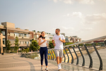 Fototapeta premium Couples enjoy a morning jog along a scenic waterfront pathway under a bright sky in a vibrant urban landscape