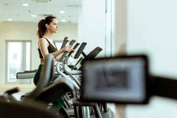 Determined young woman training on elliptical machine in modern gym during morning workout session