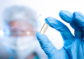 Scientist holds golden capsule while examining molecular structures in laboratory setting during...
