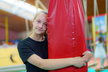 Young girl enjoys playful moment at gymnastics training center while hugging a large red mat