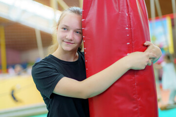 Girl enjoying gymnastic practice while hugging a red safety mat in a training facility during afternoon hours