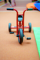 Bright red tricycle sits on a gym floor during an active children's play session in the community center