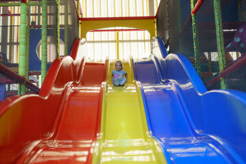 Child slides down colorful play structure in indoor playground during afternoon fun