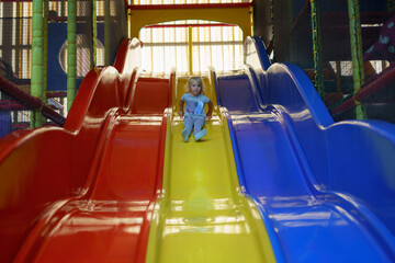 Child enjoys sliding down colorful play structure in indoor playground during afternoon