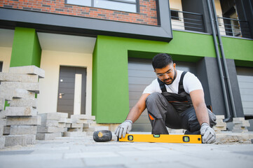 Indian master in gloves lays paving stones in layers. Garden brick pathway paving by professional...